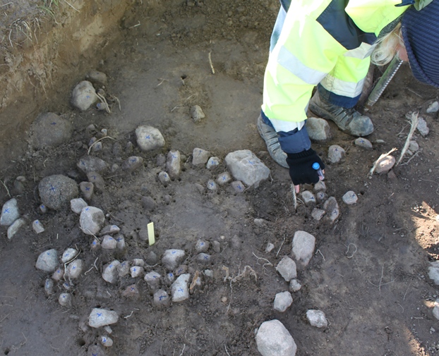 Archaeologists clearing part of the trench with Ale's Stones in the background. Credit: Annika Knarrström, Swedish National Heritage Board.